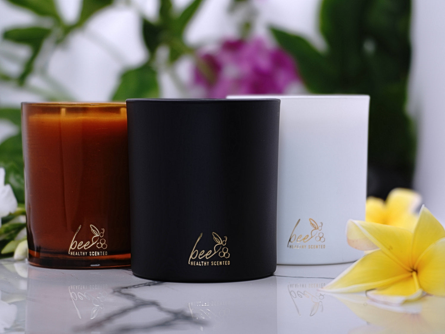 luxurious beeswax candle jars  one white , one black and one amber in a marble surface with a yellow flower